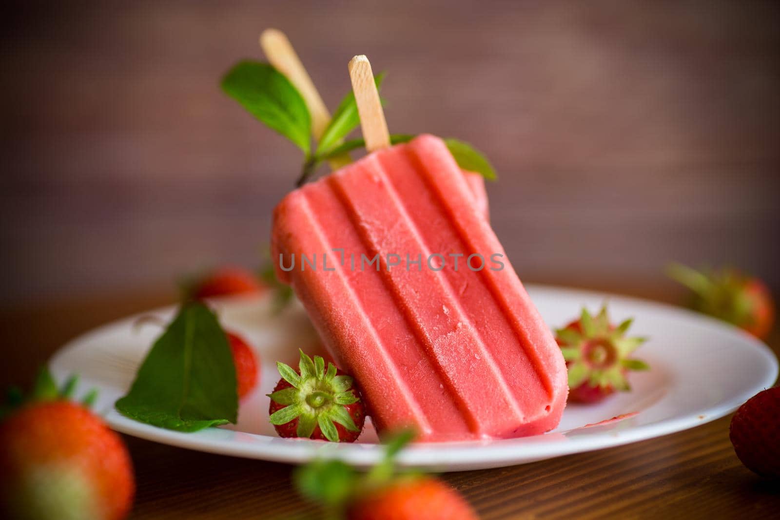 homemade strawberry ice cream on a stick made from fresh strawberries in a plate on a wooden table