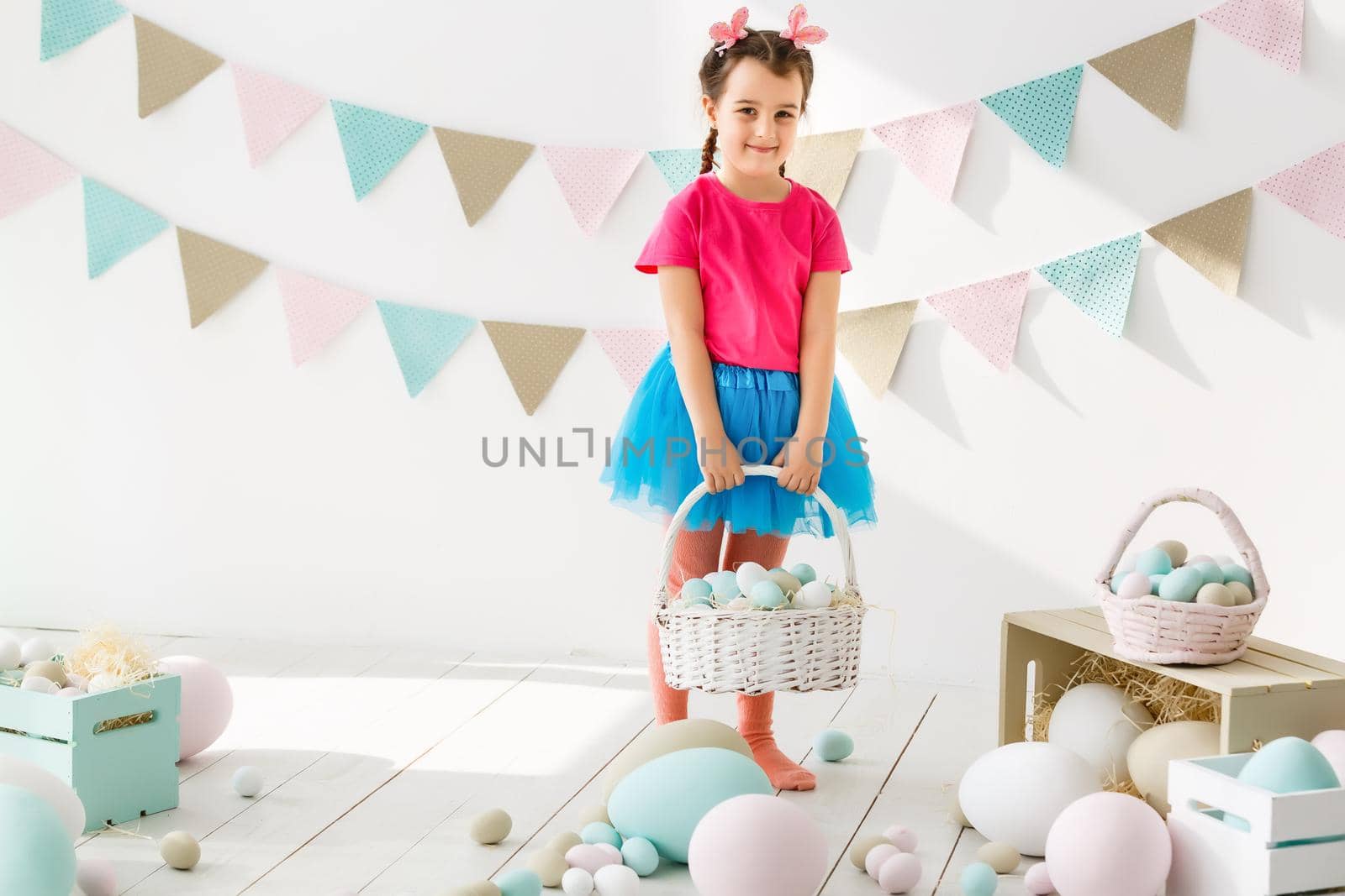 Getting ready to Easter. Lovely little girl holding an Easter egg and smiling with decoration in the background