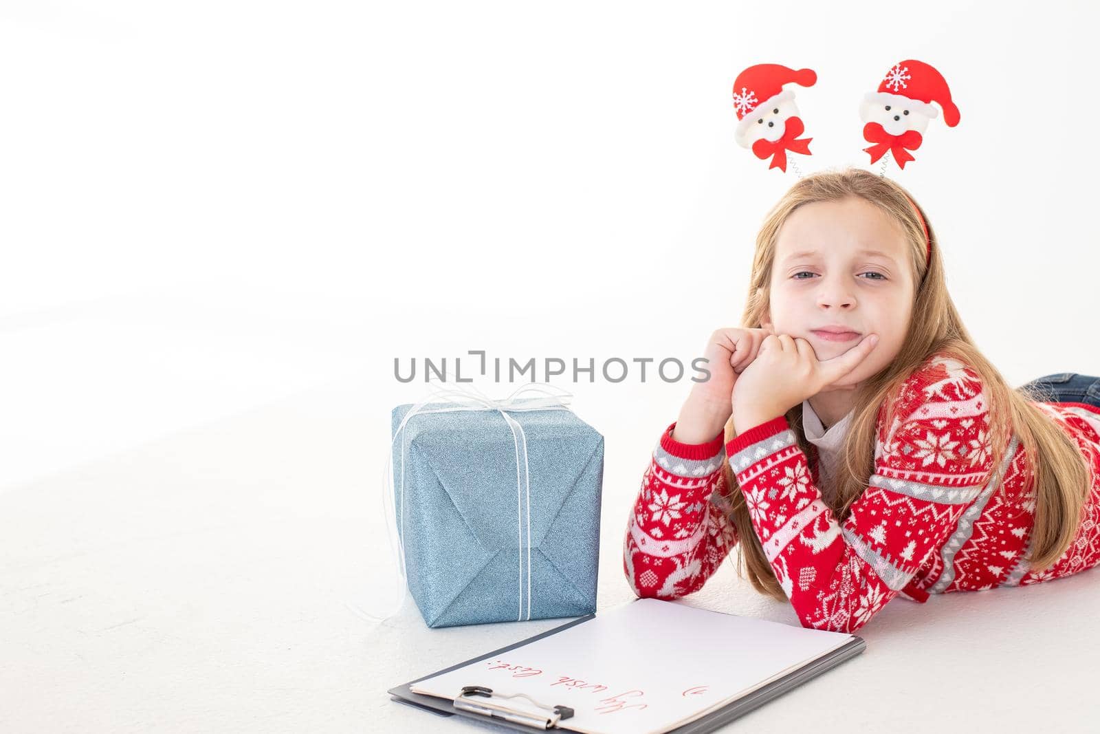 Thoughtful little girl writes letter to Santa Claus on white background.Goals plans dreams make to do list for new year christmas concept. Special orders for Santa. girl lying near the presents by YuliaYaspe1979