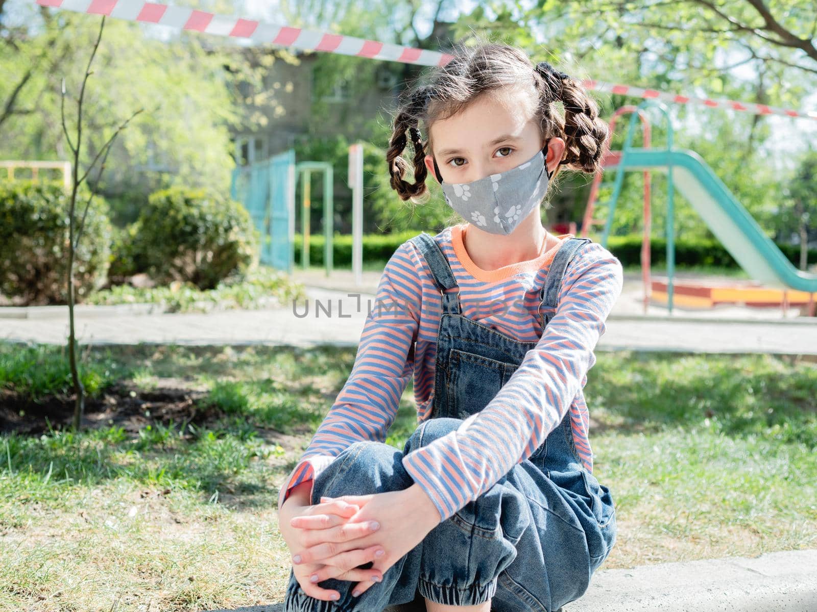 Sad little girl on the background of the closed Playground in the period of quarantine due to coronavirus infection