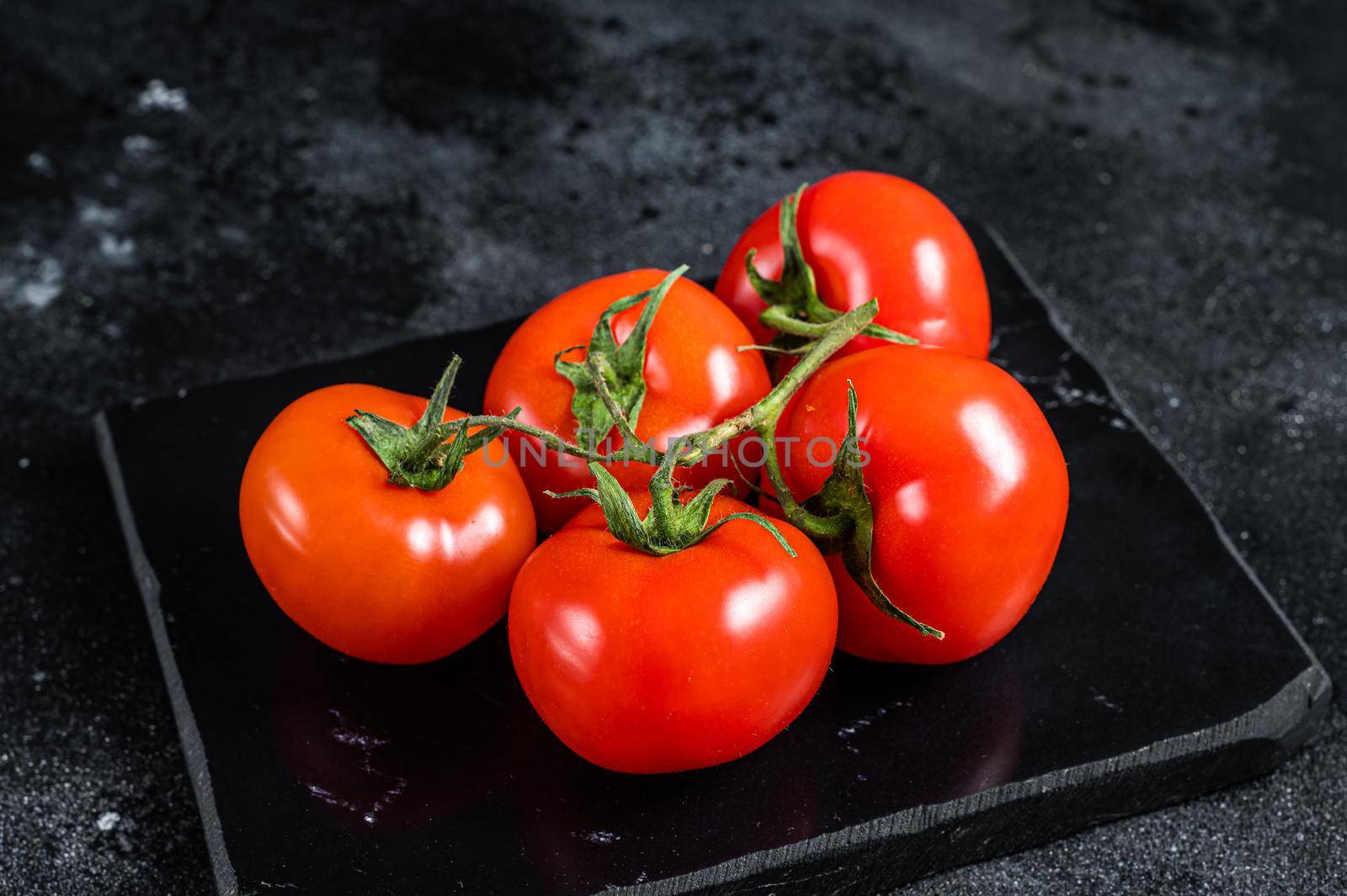 Branch of Red cherry tomatoes on marble board. Black background. Top view.