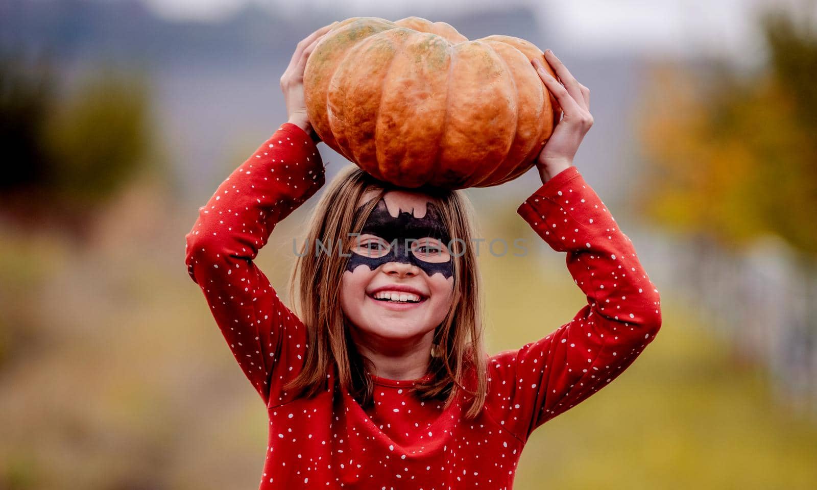 Smiling little girl holding pumpkin above head by tan4ikk1
