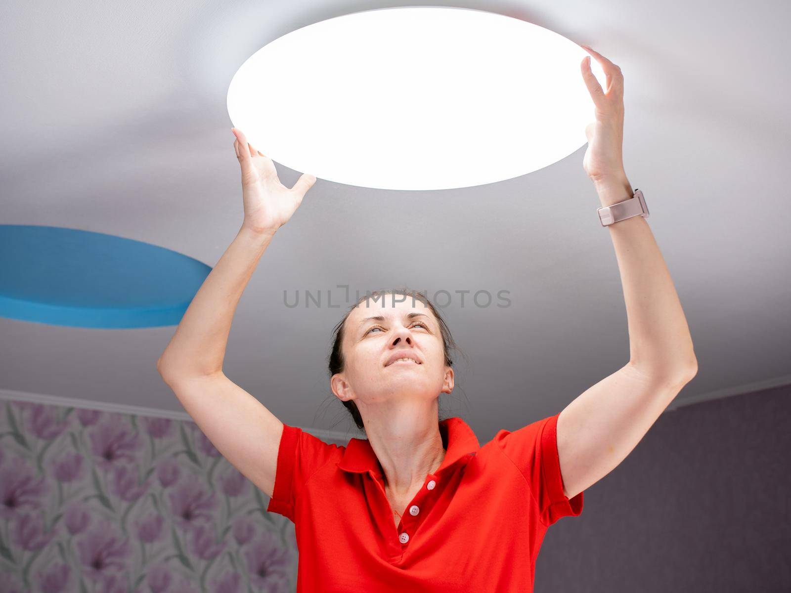 A woman in a children's room sets a ceiling lamp.