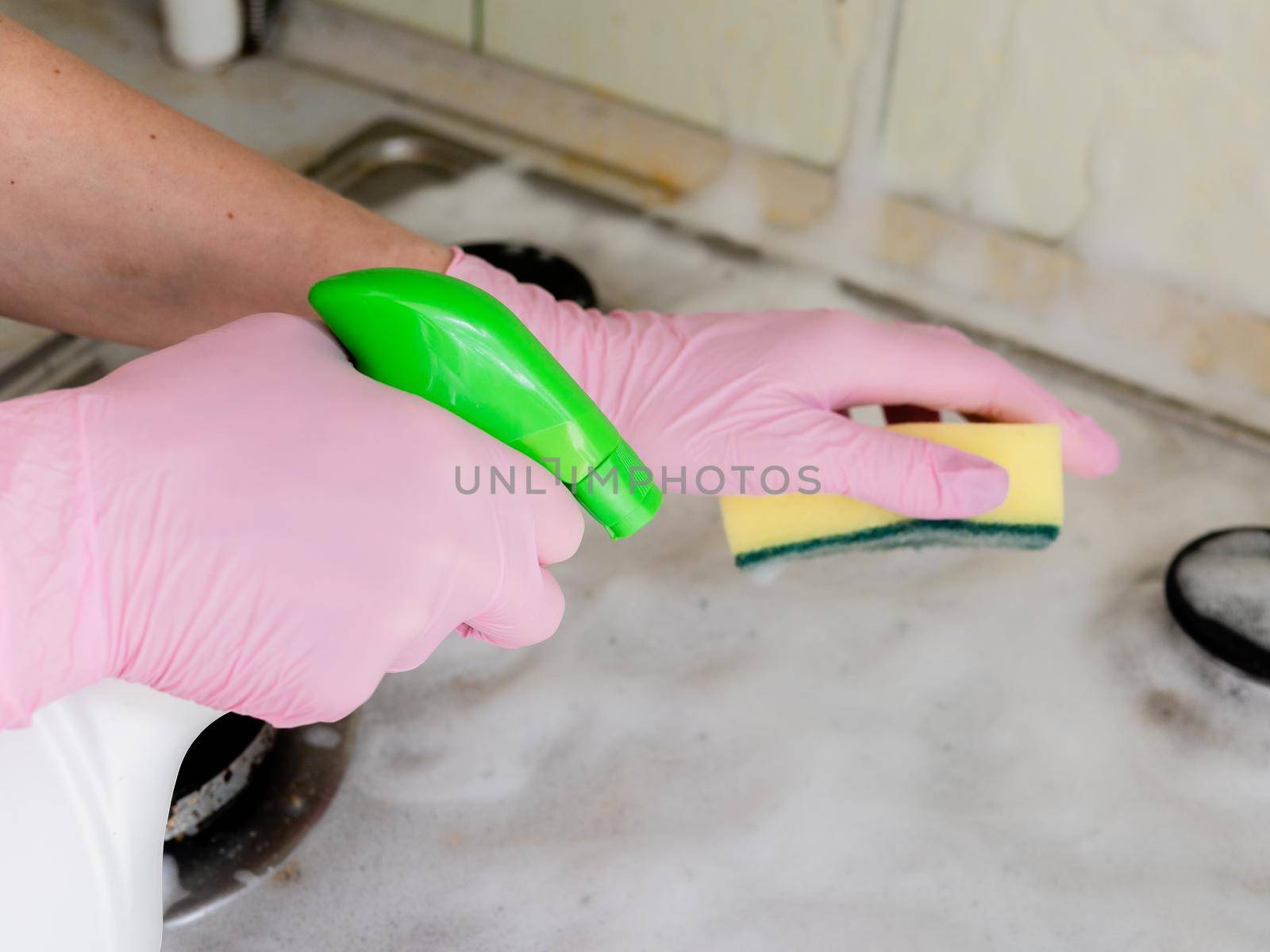 A woman in pink gloves washes the gas stove with a washcloth and detergent. by Utlanov