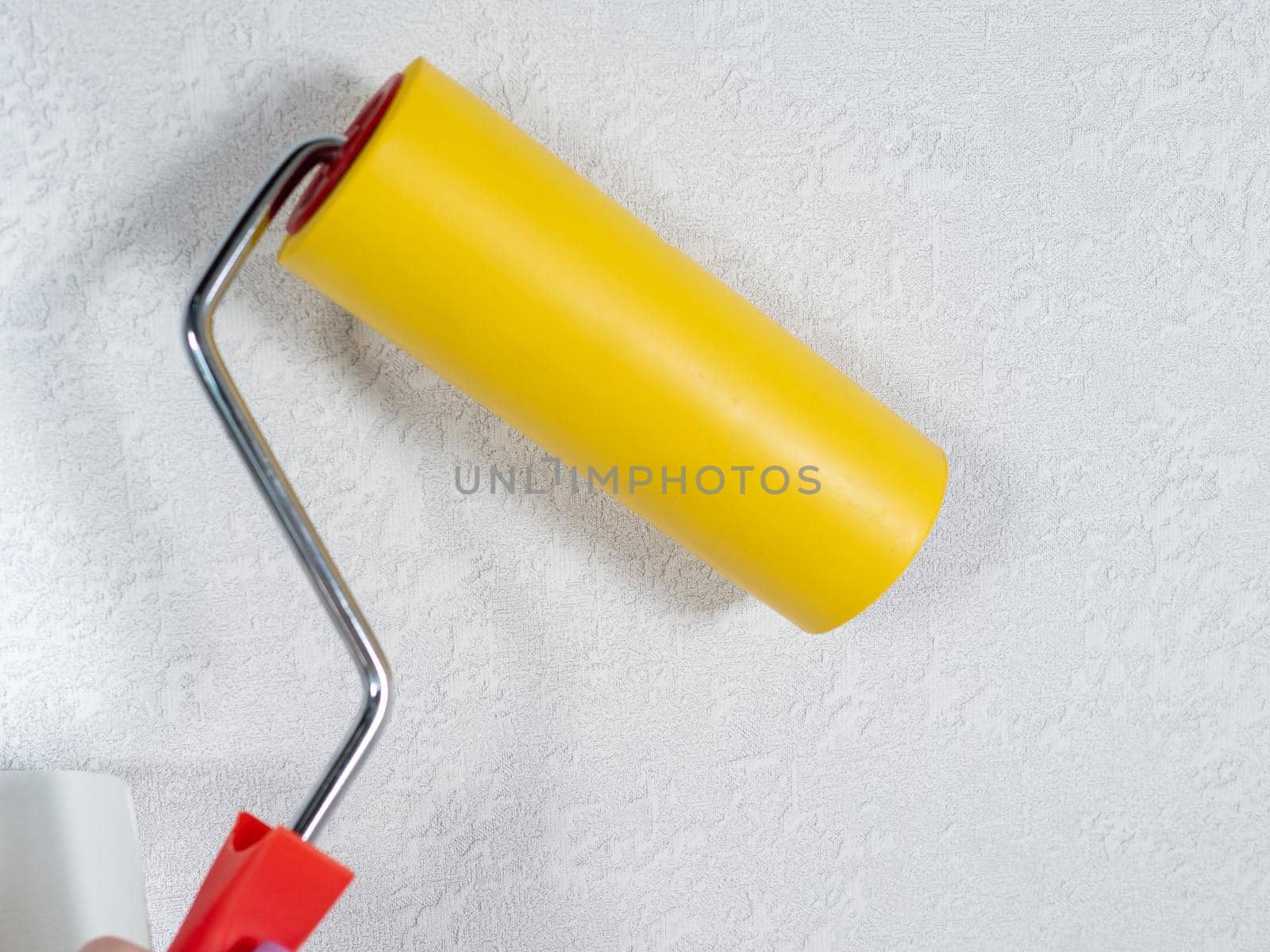 Roller for smoothing wallpaper yellow. Paint roller with a red handle and a yellow smooth nozzle on a light background. Wallpapering in the apartment.