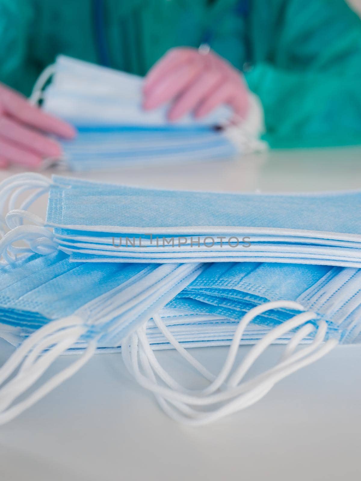 A doctor wearing disposable blue gloves takes a stack of medical masks from a light table and counts their number. by Utlanov