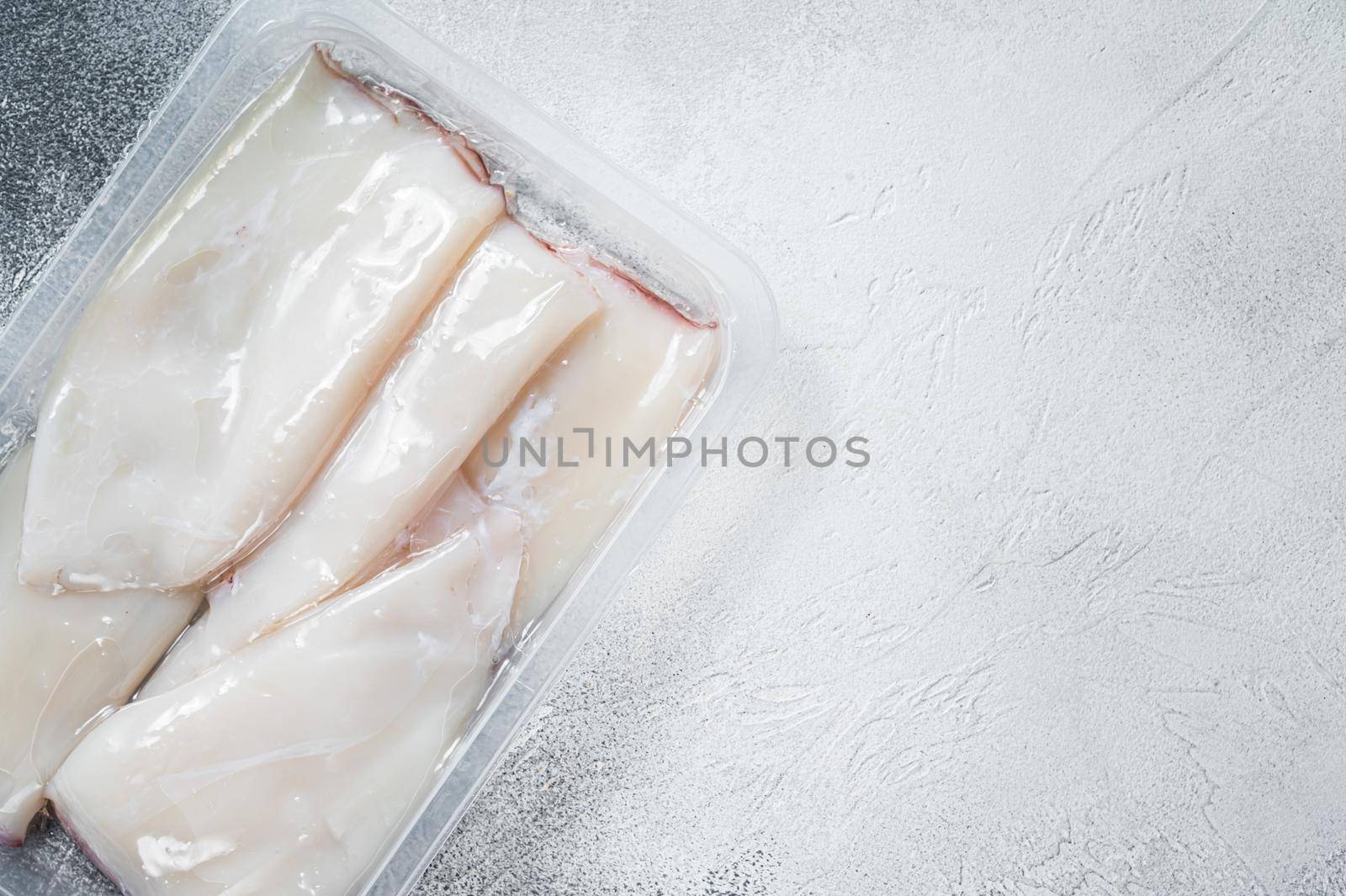 Fresh Raw Squid or Calamari in a vacuum package on a kitchen table. White background. Top view. Copy space by Composter