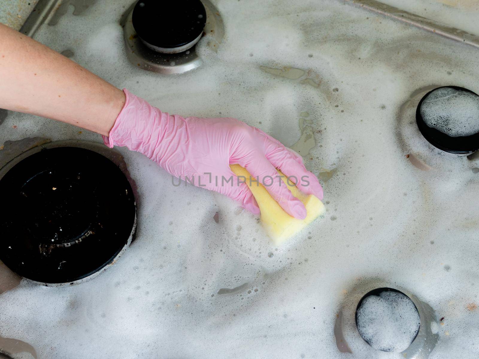 Close-up, a washcloth in the hands of gloved hands carefully washes the gas stove.