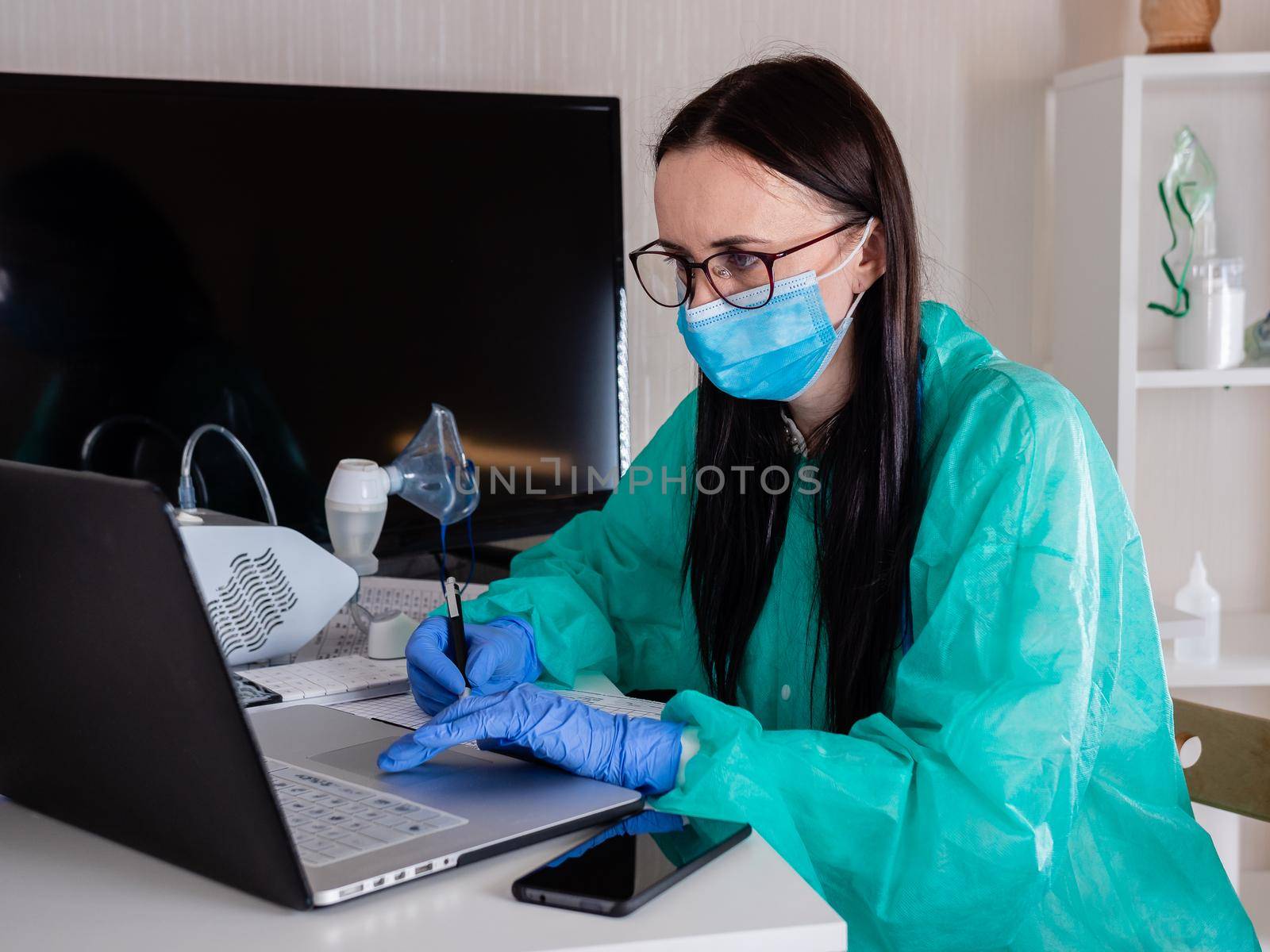 A woman in a protective mask sits at the workplace and works with documents at the computer.