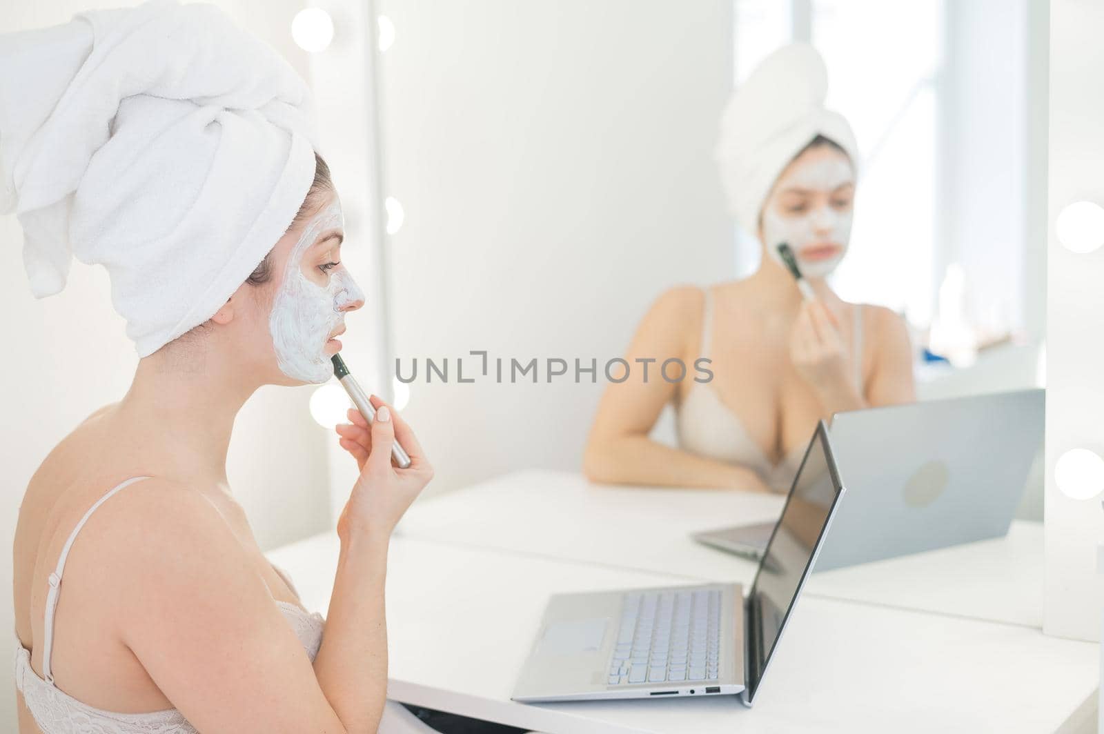 Caucasian woman applying face mask and looking at laptop manual