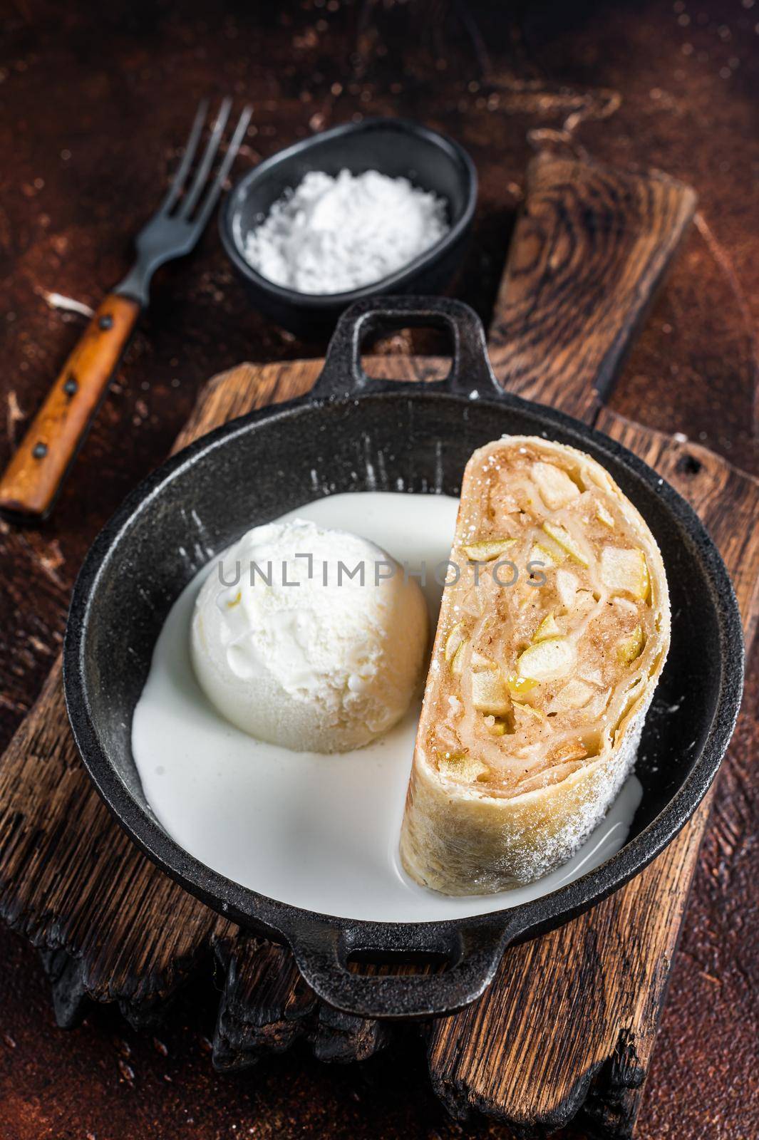 Apfelstrudel strudel with cinnamon, powdered sugar and vanilla ice cream in a pan. Dark background. Top view.