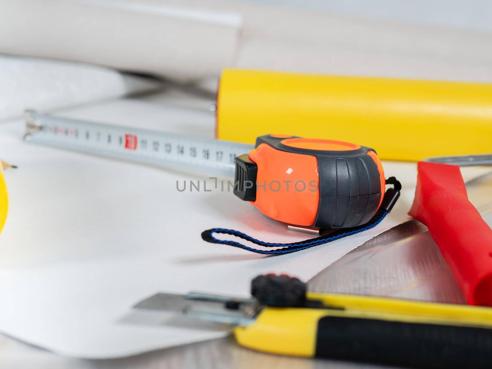 Close-up the measuring tape and the Wallpaper smoothing roller are lying on the floor next to the Wallpaper roll. by Utlanov