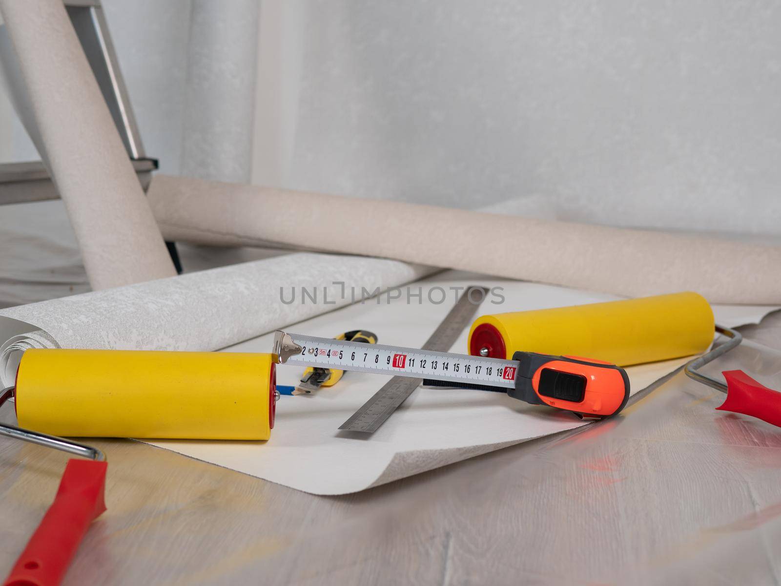 Close-up the measuring tape and the Wallpaper smoothing roller are lying on the floor next to the Wallpaper roll. by Utlanov