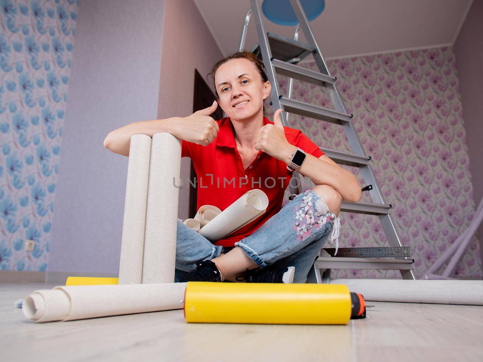 A woman is sitting on the floor in a room with rolls of Wallpaper. Concept of renovation in the apartment. by Utlanov