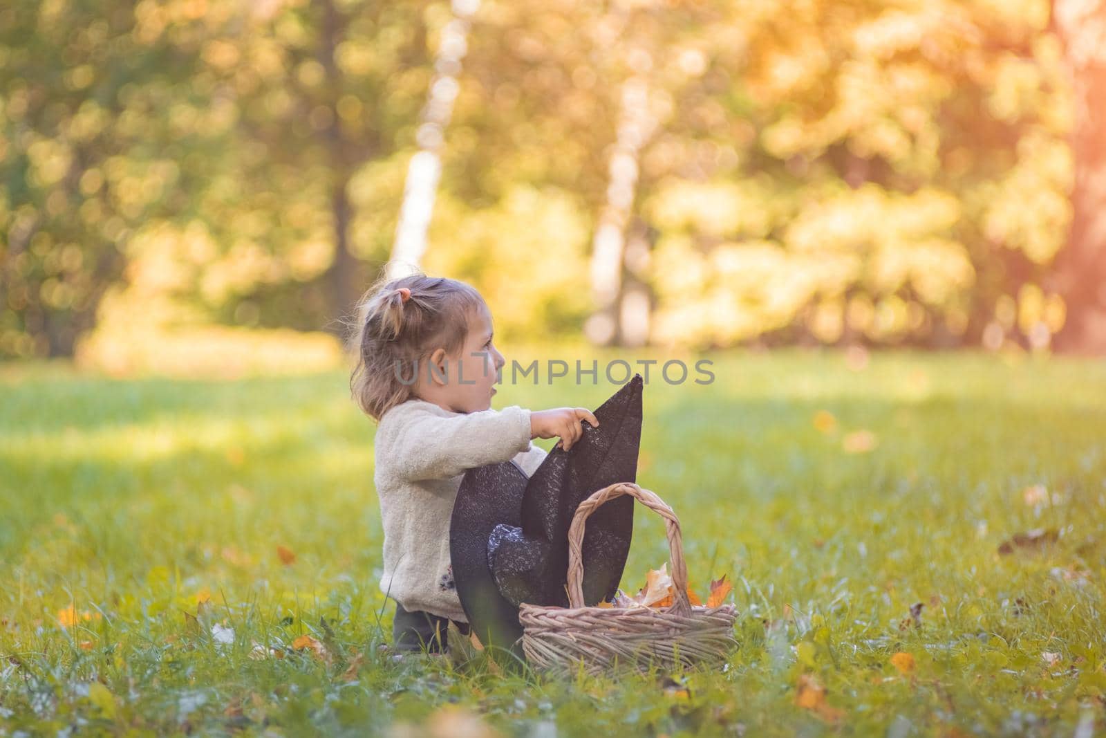 halloween celebration concept. cute toddler playing with witch hat on the lawn in the autumn park on a sunny day.