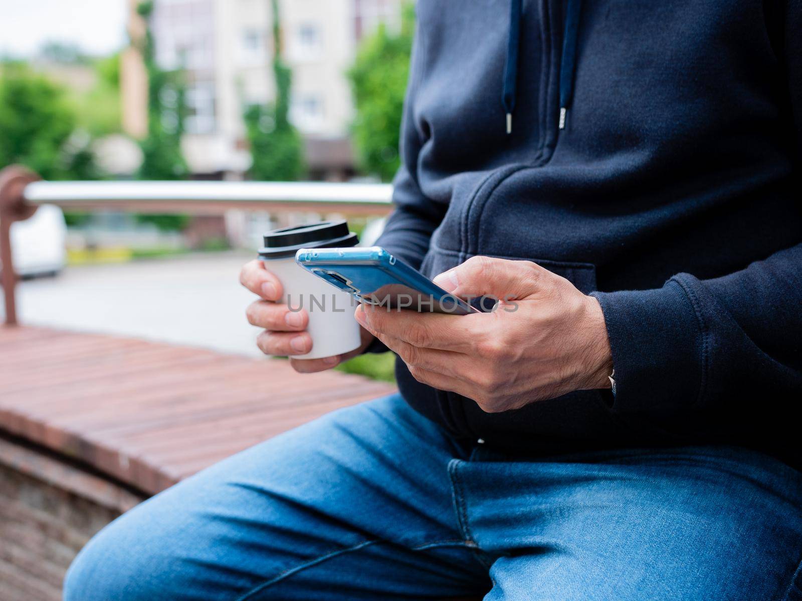 Close-up of hands of a man with coffee in a paper Cup and a smartphone. by Utlanov