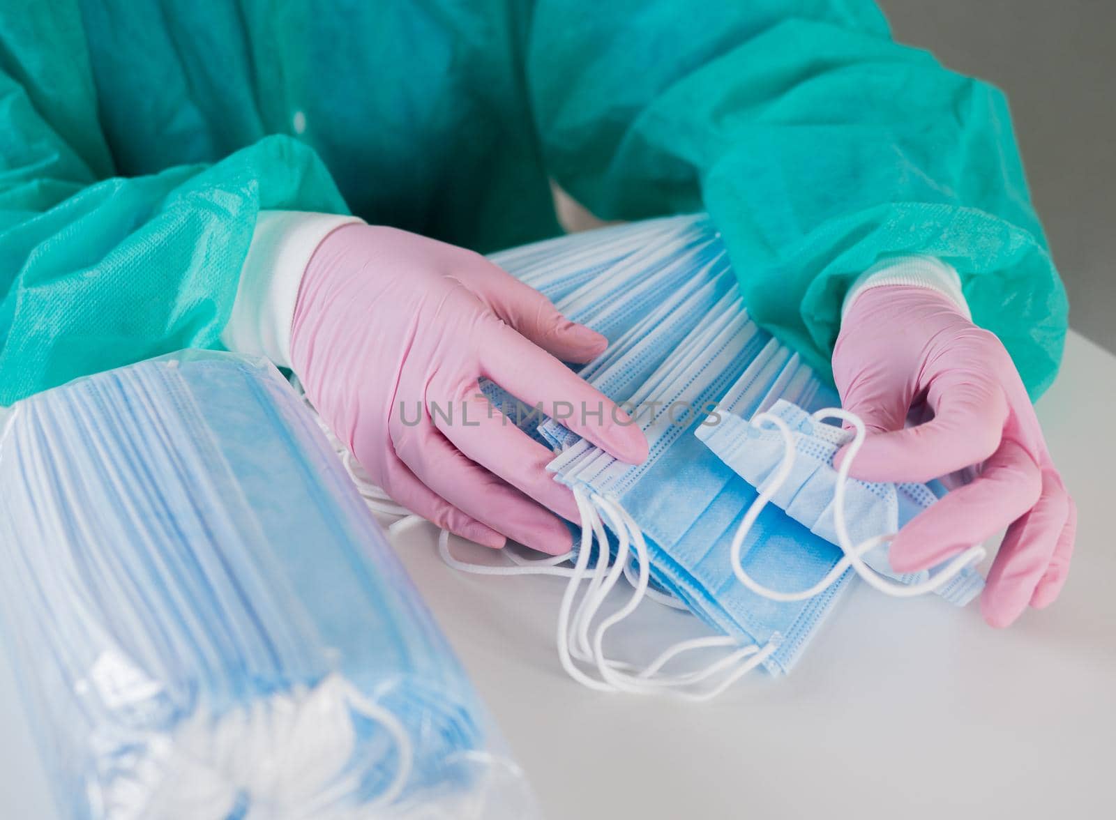 A doctor wearing disposable blue gloves takes a stack of medical masks from a light table and counts their number. by Utlanov