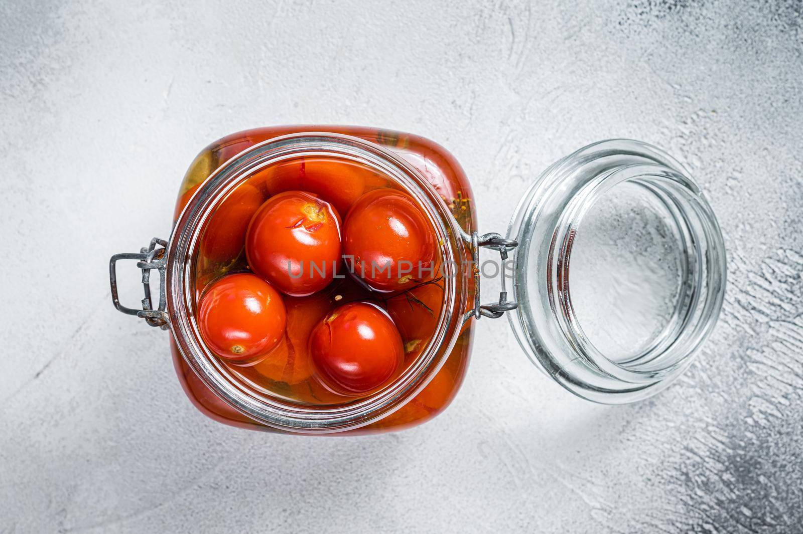 Pickled cherry tomatoes in a glass jar. White background. Top view.