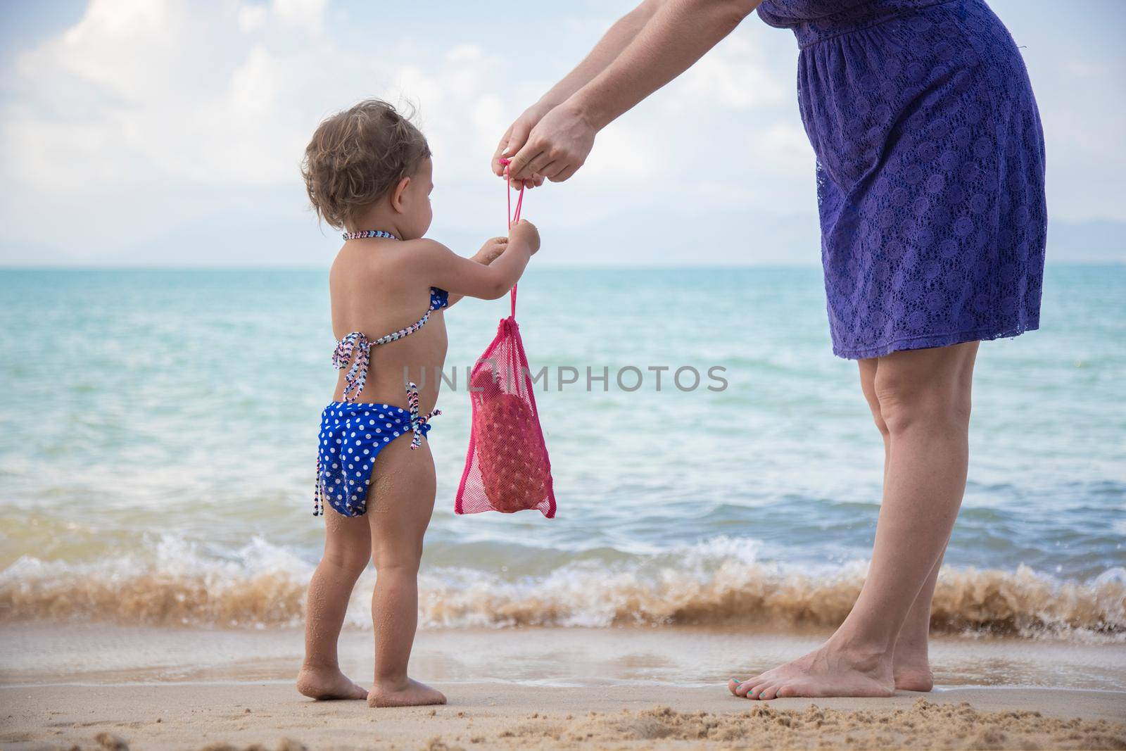 mom gives her child a mesh bag on the sea beach. ecology culture since an early age