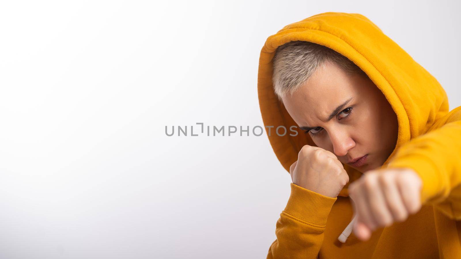 Young woman in ocher hood holding fists near face on white background. Boxer girl is ready for a fight