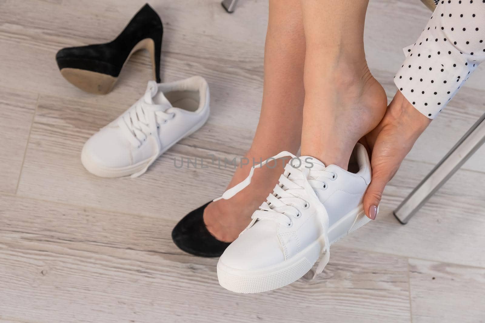 Close-up business woman takes off her shoes puts on white leather sneakers