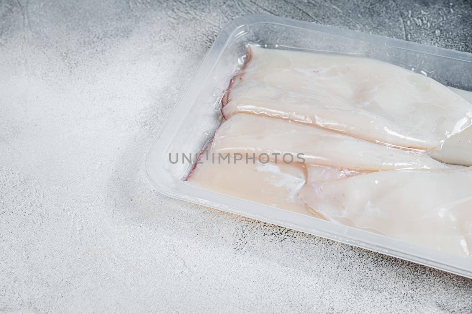 Raw squid or Calamari in a vacuum package from the supermarket. White background. Top view. Copy space by Composter