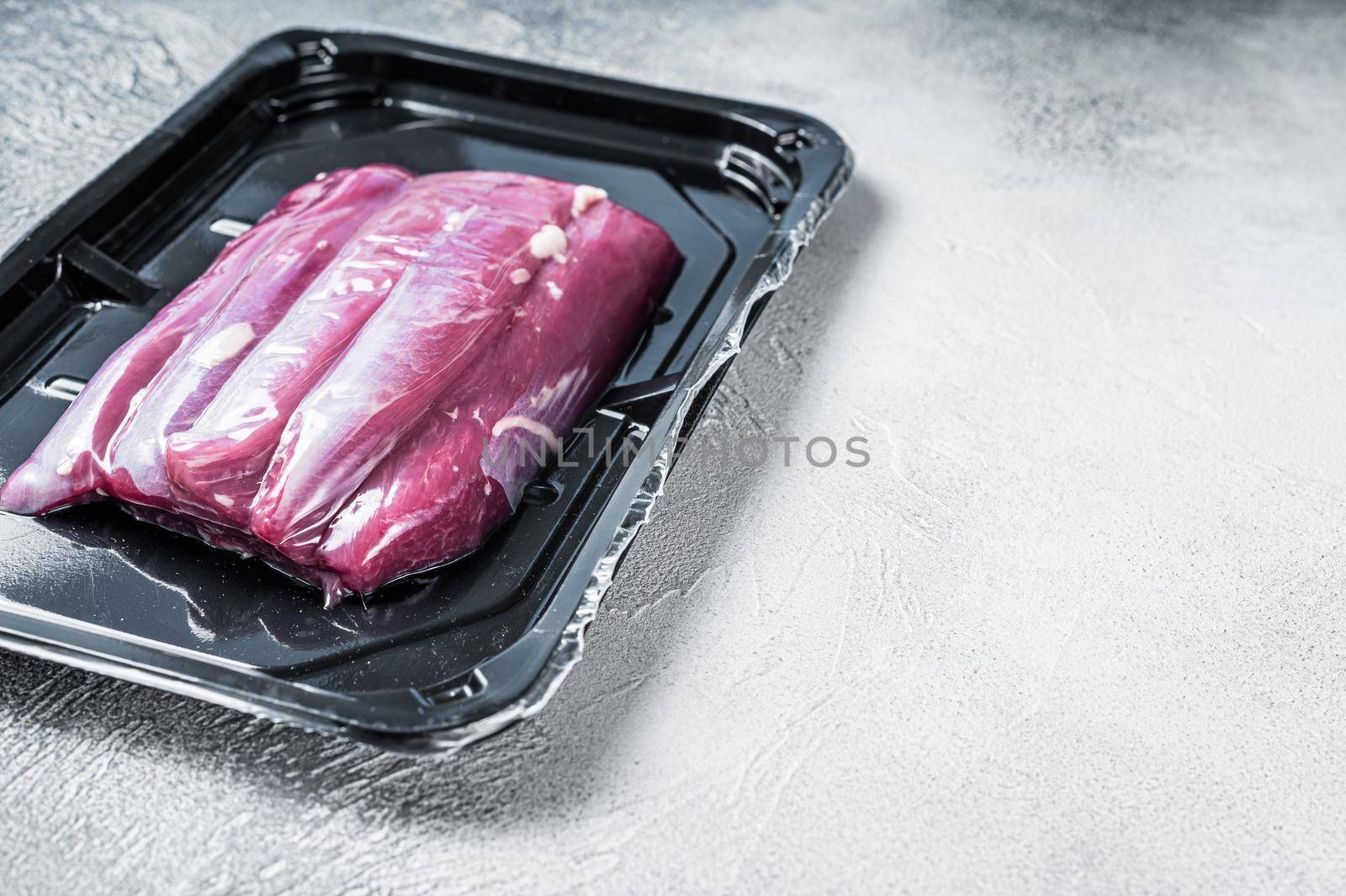 Raw lamb tenderloin in vacuum packaging. White background. Top view. Copy space by Composter