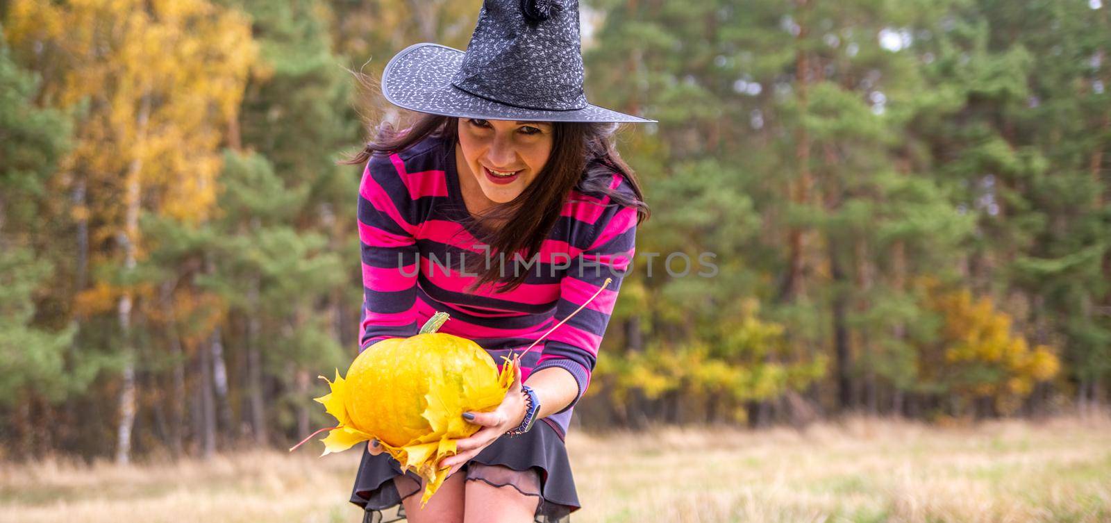 Young witch with pumpkin and leaves in the autumn forest. halloween concept