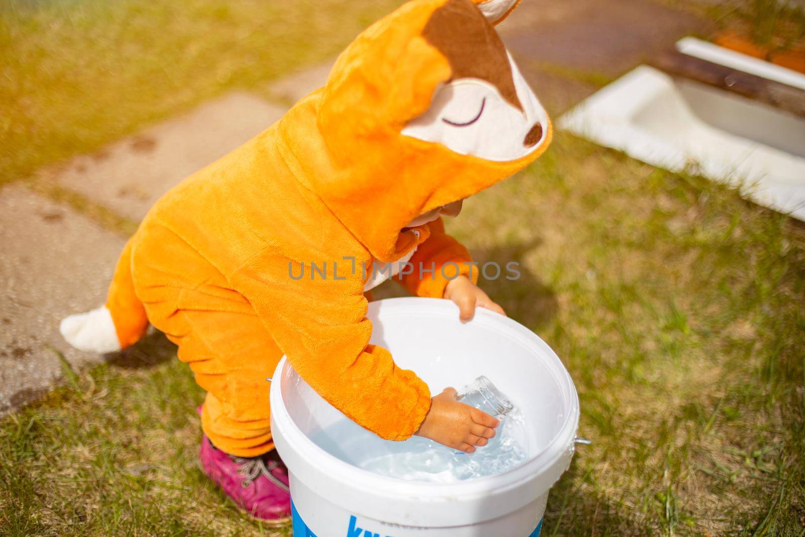 adorable little toddler playing with water in the backyard in sunshine. child in a fox costume