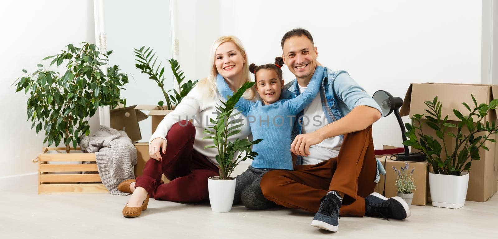 Happy family sitting on wooden floor. Father, mother and child having fun together. Moving house day, new home and design interior concept