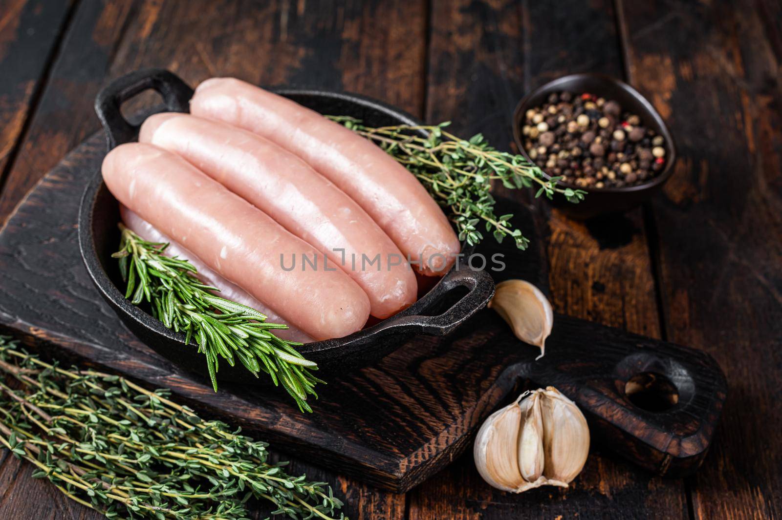 Pork raw sausages in a pan with herbs. Dark wooden background. Top view.