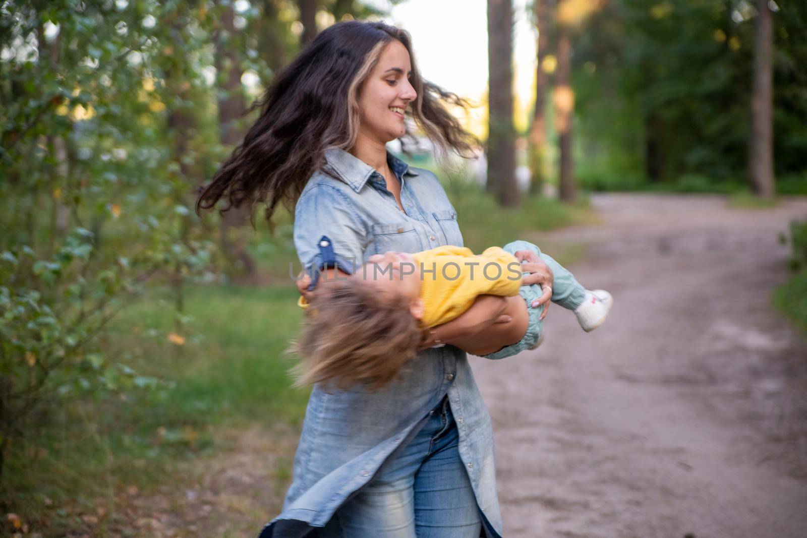 young mother is spinning with a baby in her arms. happy mom dancing with toddler on the background of nature and forest. mom and daughter laugh. carefree parenthood
