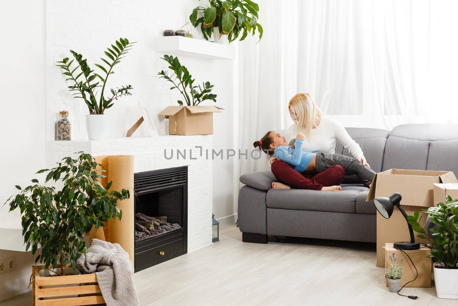 Cute mother and little daughter are on floor near boxes. They are preparing to move in another building. The parent and child are relaxing and smiling