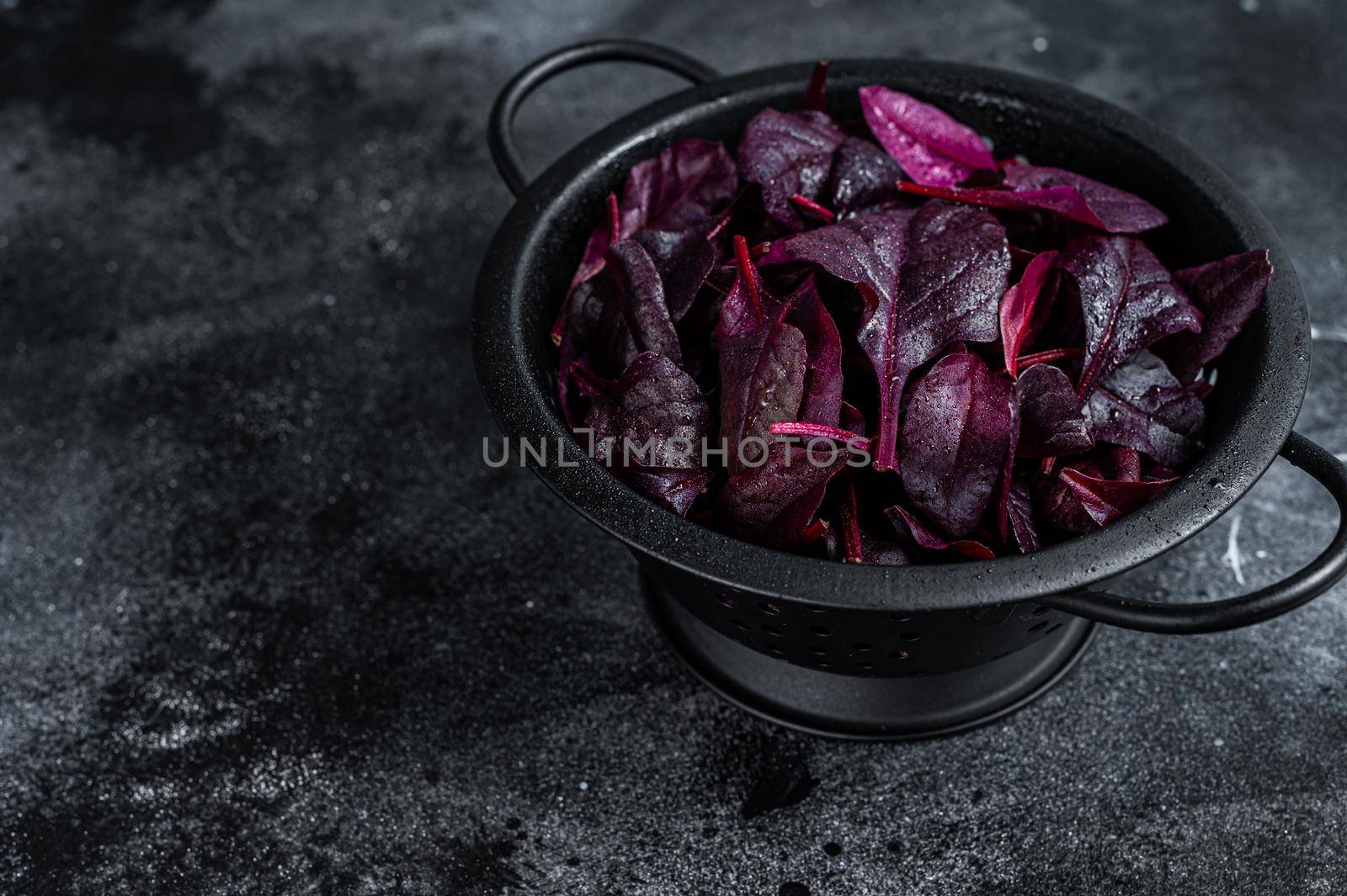 Leaves of Swiss red chard or Mangold salad in a colander. Black background. Top view. Copy space by Composter