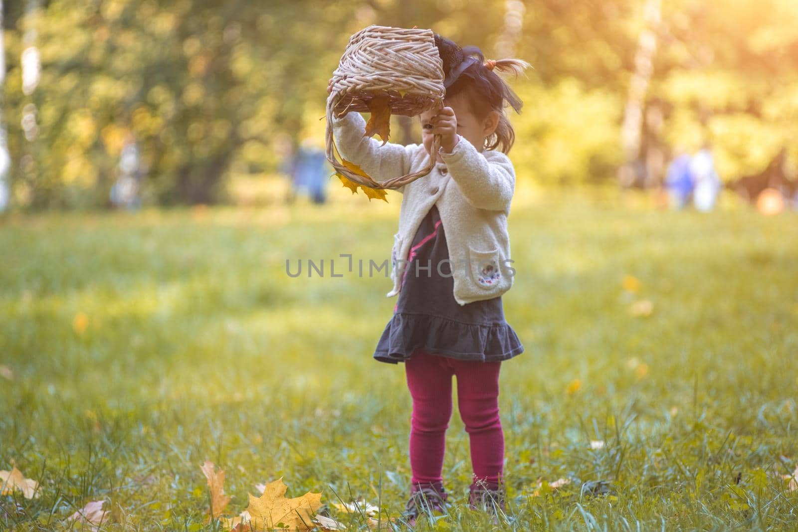 little cute witch flips a basket and pours autumn leaves in the park