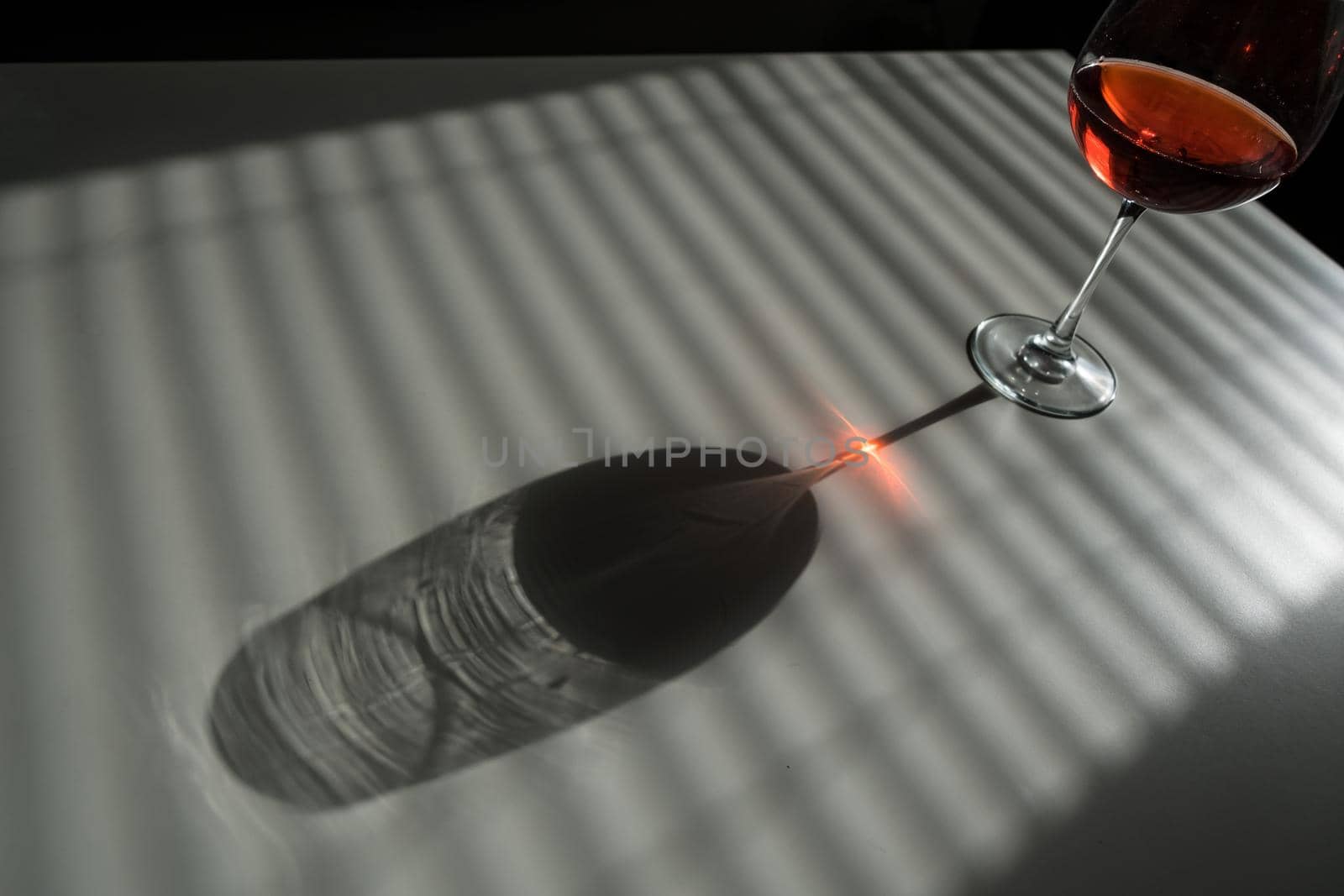 A glass of red wine on a white table with a shade from the blinds.