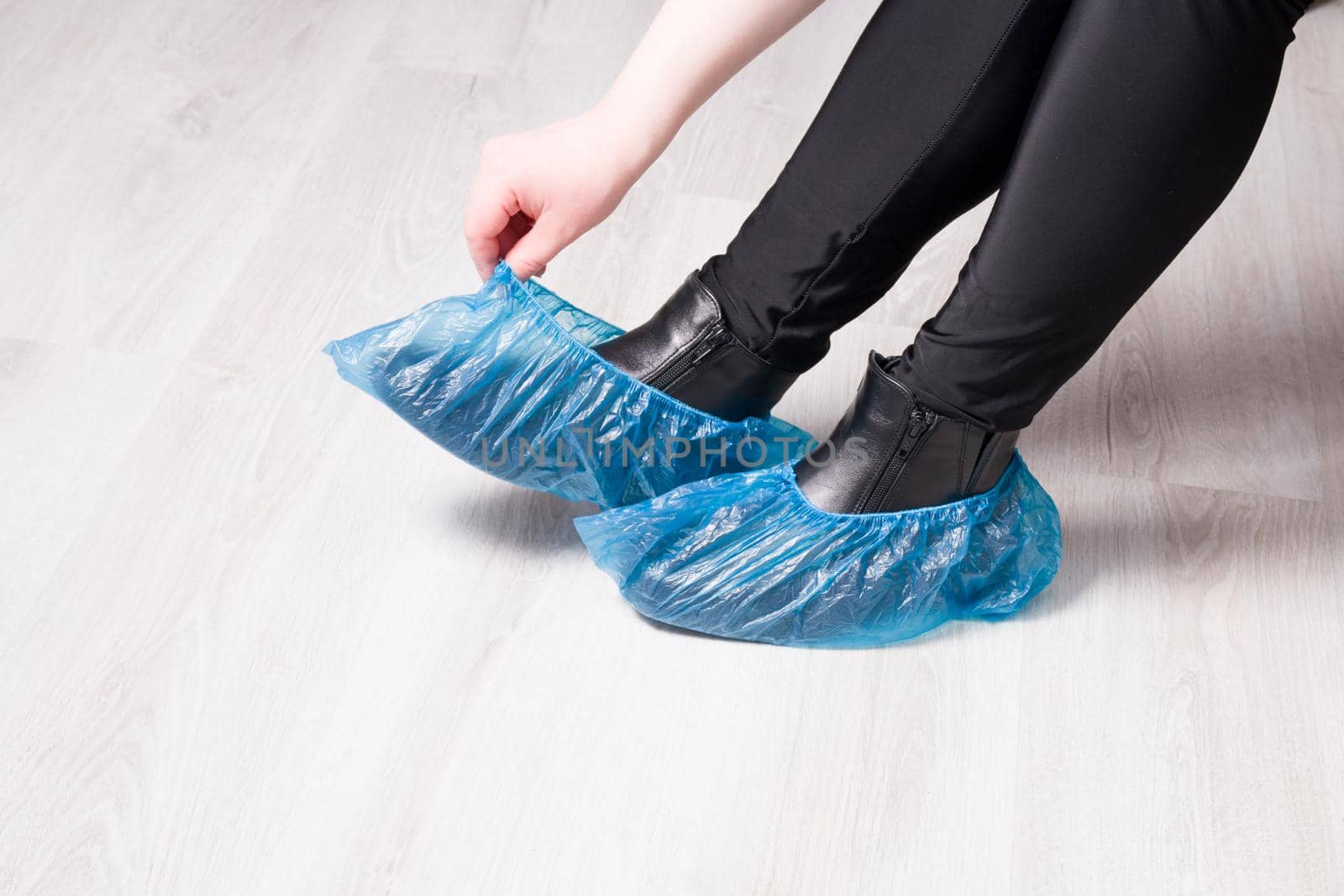 a woman in black trousers sits and takes off her shoe covers, black leather boots, light wooden floor, copy space