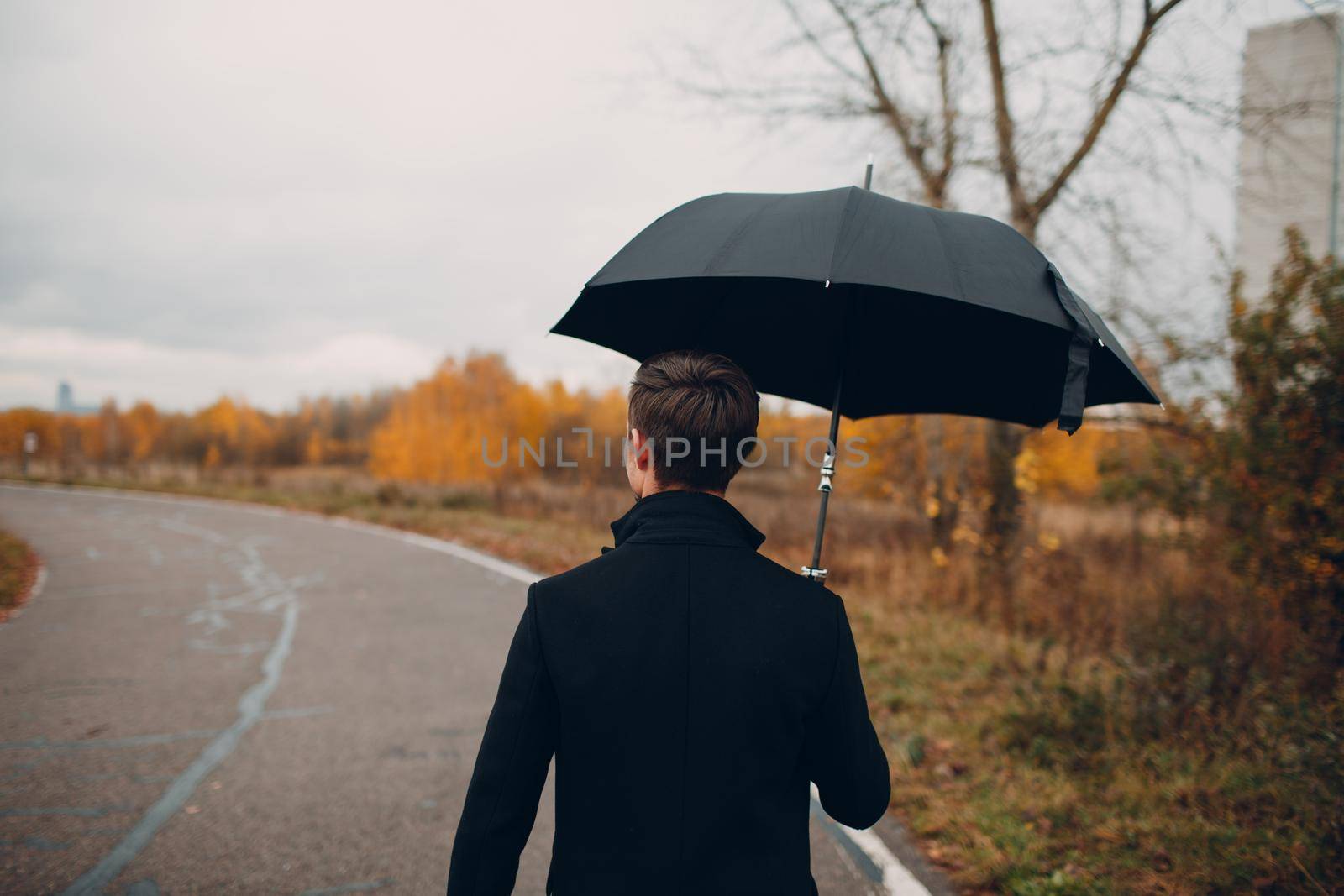 Young man in black coat walking in the rain with umbrella