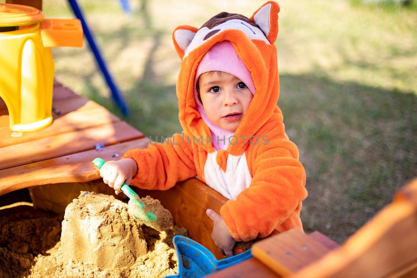 adorable toddler playing in the sandbox. cute child in fox pajamas plays in the sand. portrait of a happy baby