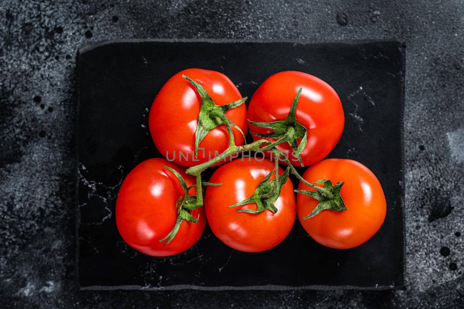 Branch of Red cherry tomatoes on marble board. Black background. Top view by Composter