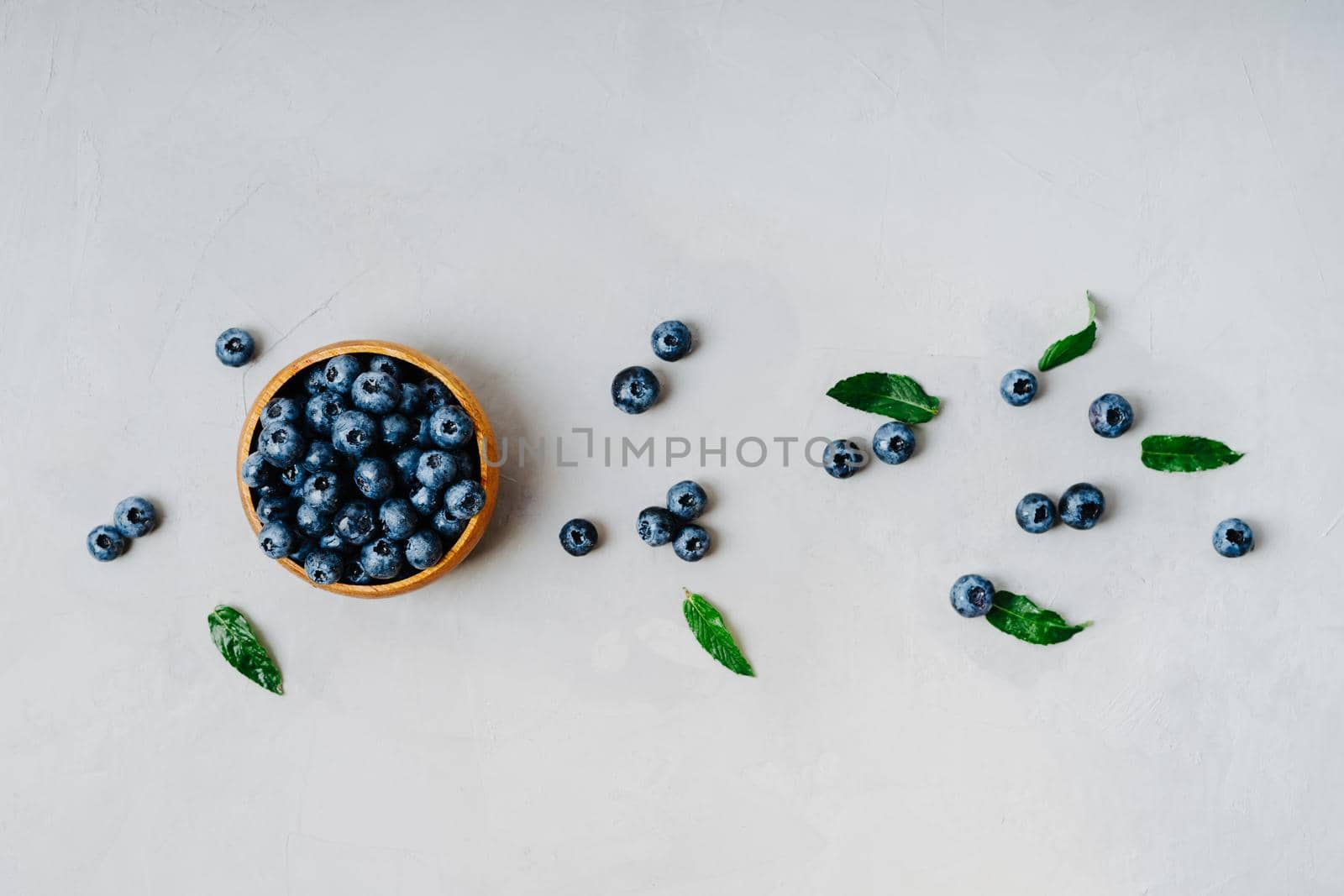 Blueberries are scattered on a gray table. Berries on a gray textured background. Top view of a bowl of blueberries. Fresh mint. The concept of healthy eating and nutrition.