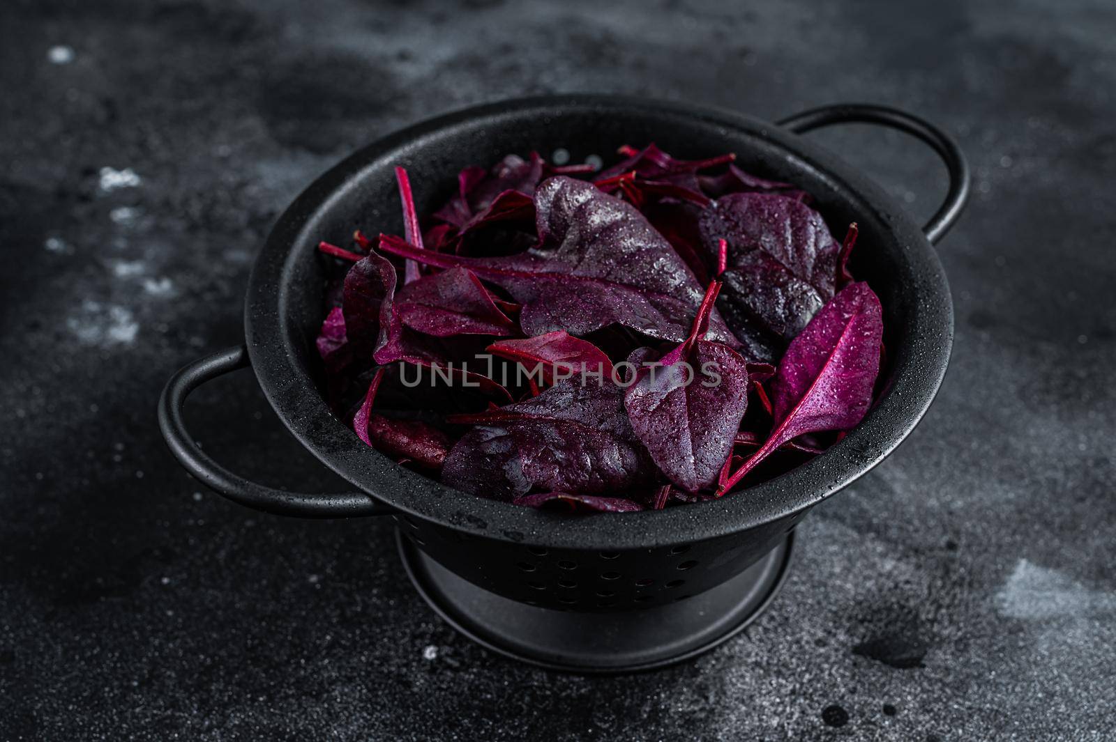 Leaves of Swiss red chard or Mangold salad in a colander. Black background. Top view.