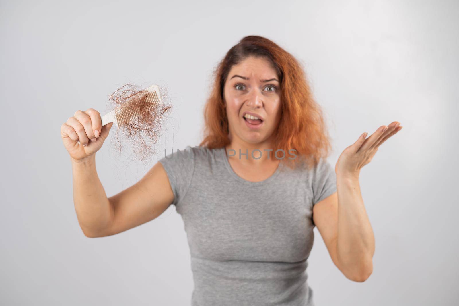 Caucasian woman with a grimace of horror holds a comb with a bun of hair. Hair loss and female alopecia. by mrwed54
