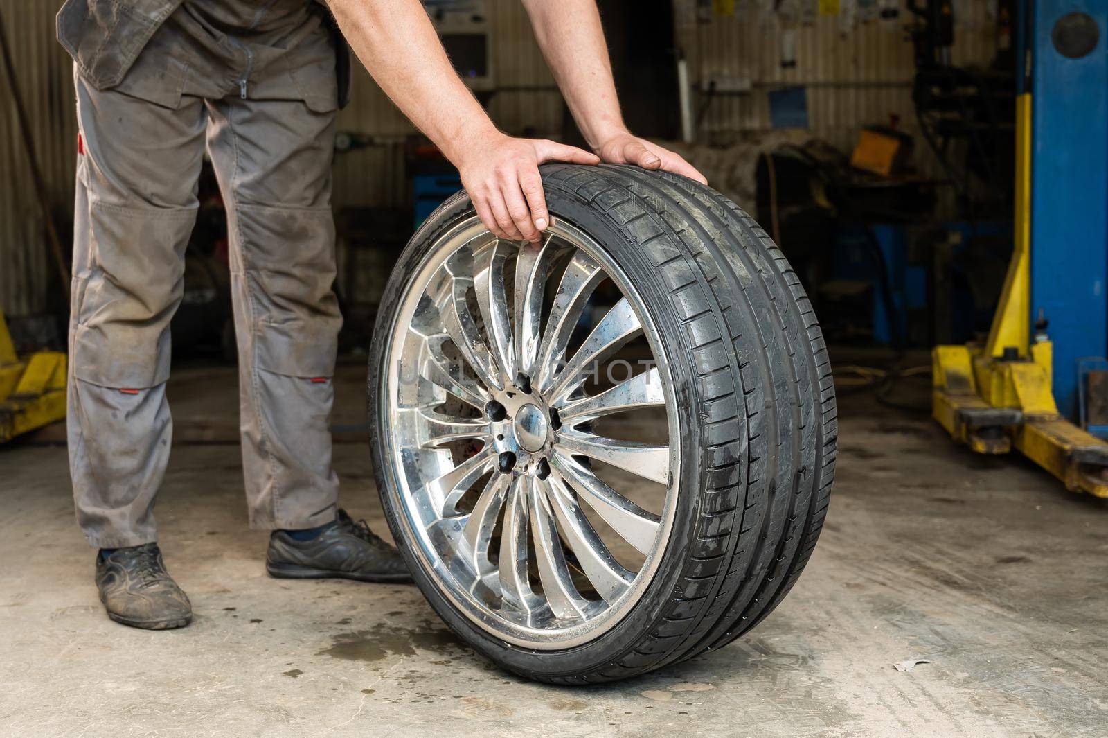 An auto mechanic holds a wheel of a car. Change of car tires according to the season.