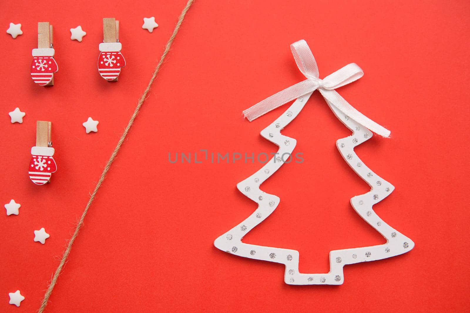 Christmas decorations decorative background. Pins in the form of red gloves and wooden Christmas tree toy in the shape of a Christmas tree on a red background. Top view, minimalism, Space for text.