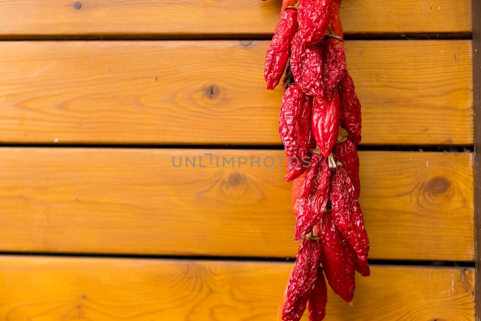 Red chili peppers on the background of the old wooden wall.string of Fresh organic peppers is hanging outside and dry in the sun. dried pepper decoration on wall. The famous Hungarian hot peppers. by YuliaYaspe1979