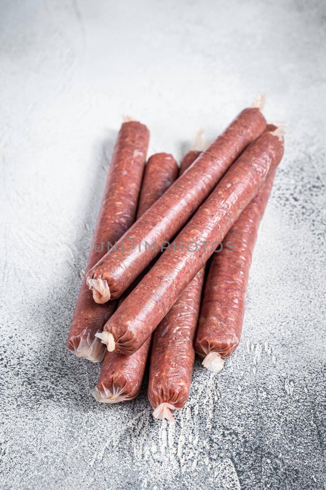 Raw butchers sausages in skins with herbs on kitchen table. White background. Top view by Composter