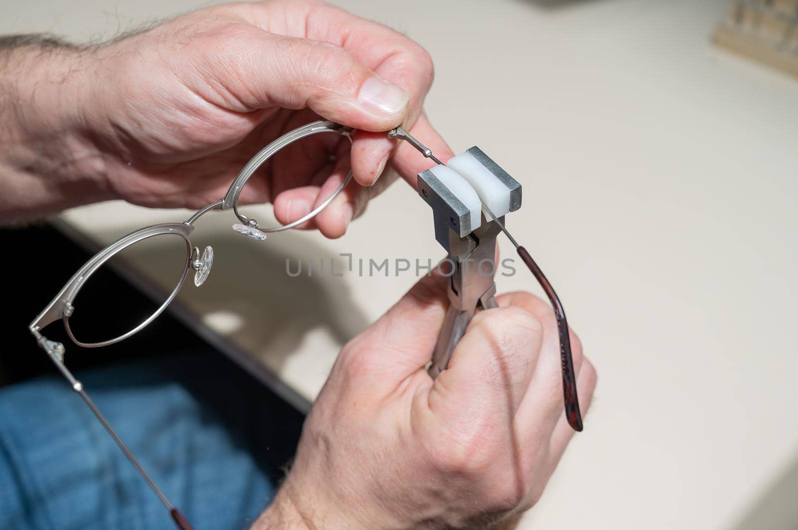 The man bends the temples of his glasses. The master repairs the frame with tongs