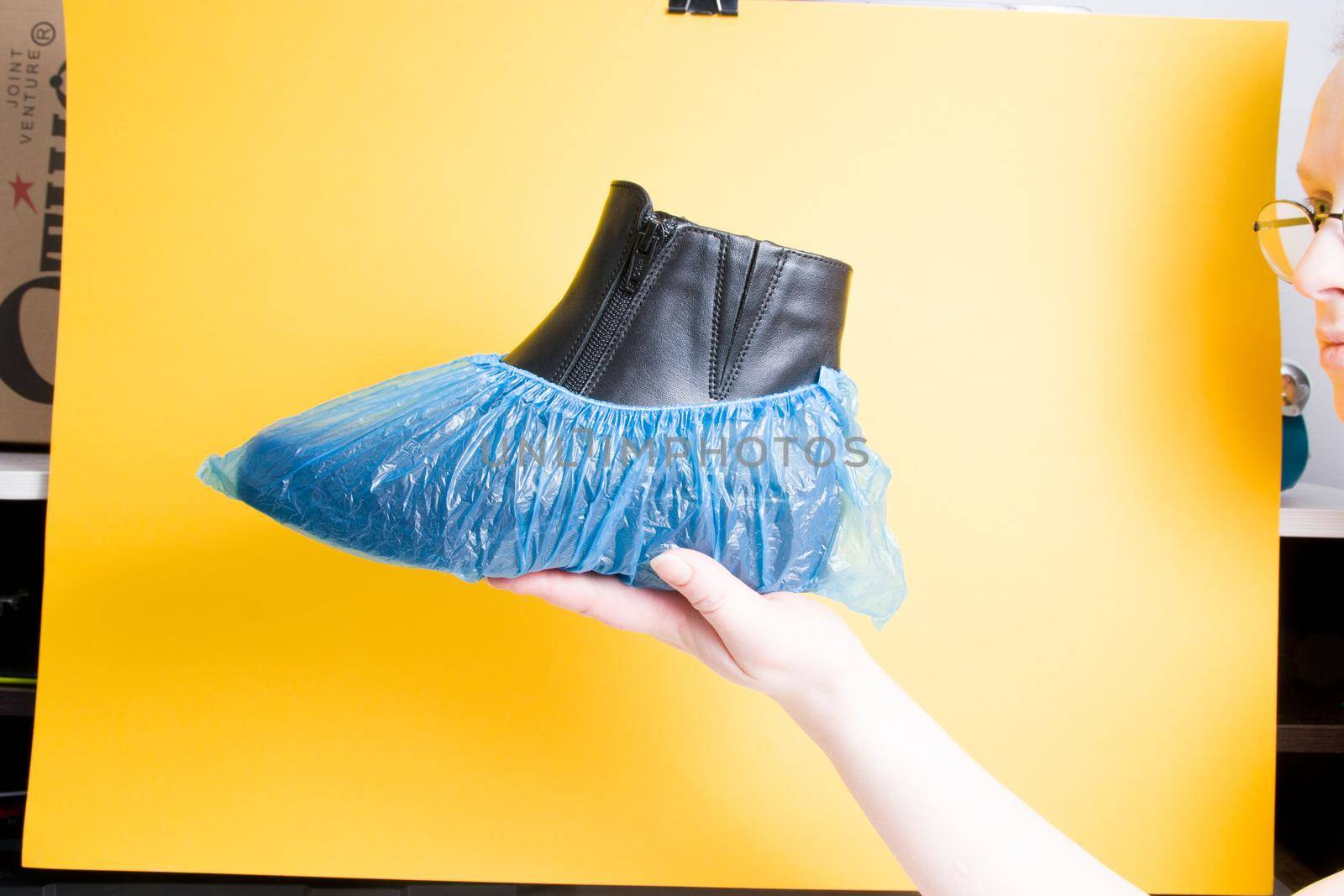 female hand holds a black leather female boot in boot covers, yellow background