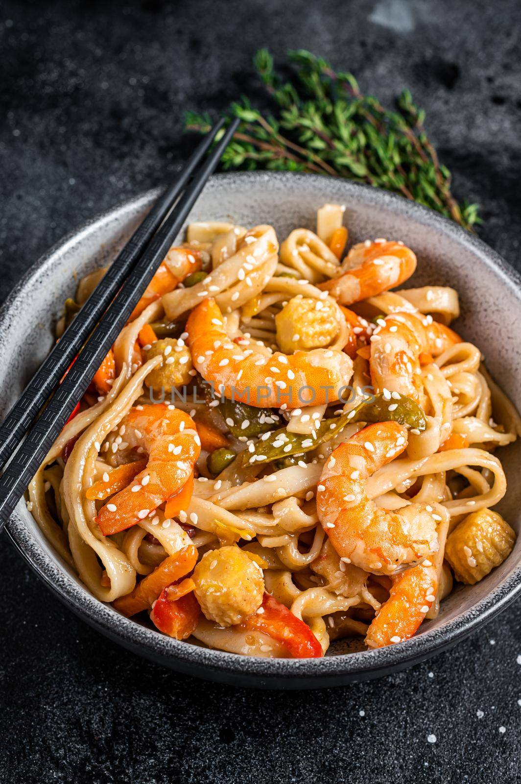 Stir-fry udon seafood noodles with shrimp prawns in a bowl. Black background. Top view by Composter